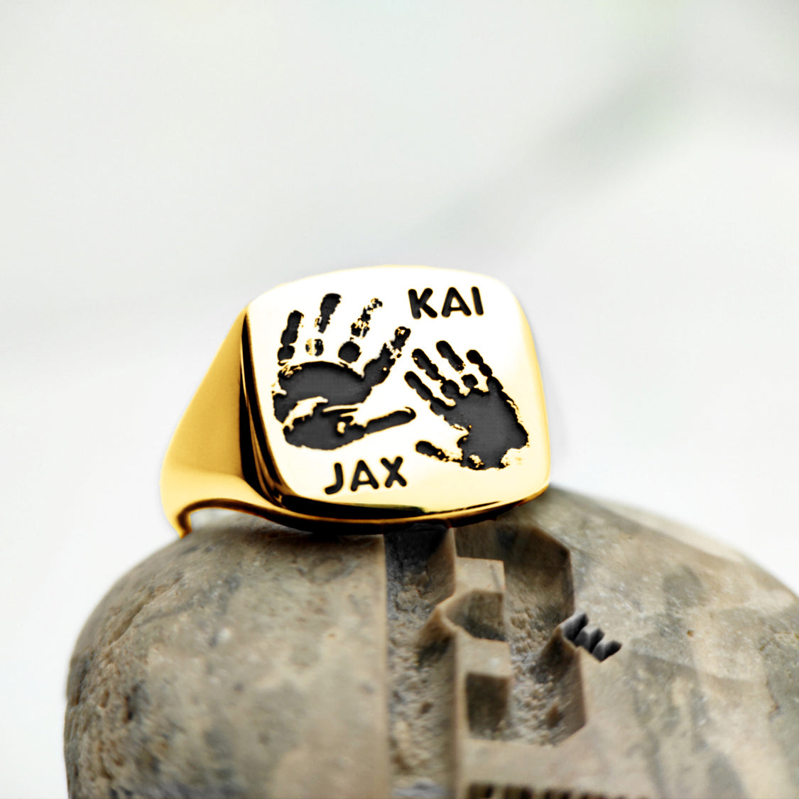 Gold signet ring engraved with black handprints Kai and Jax