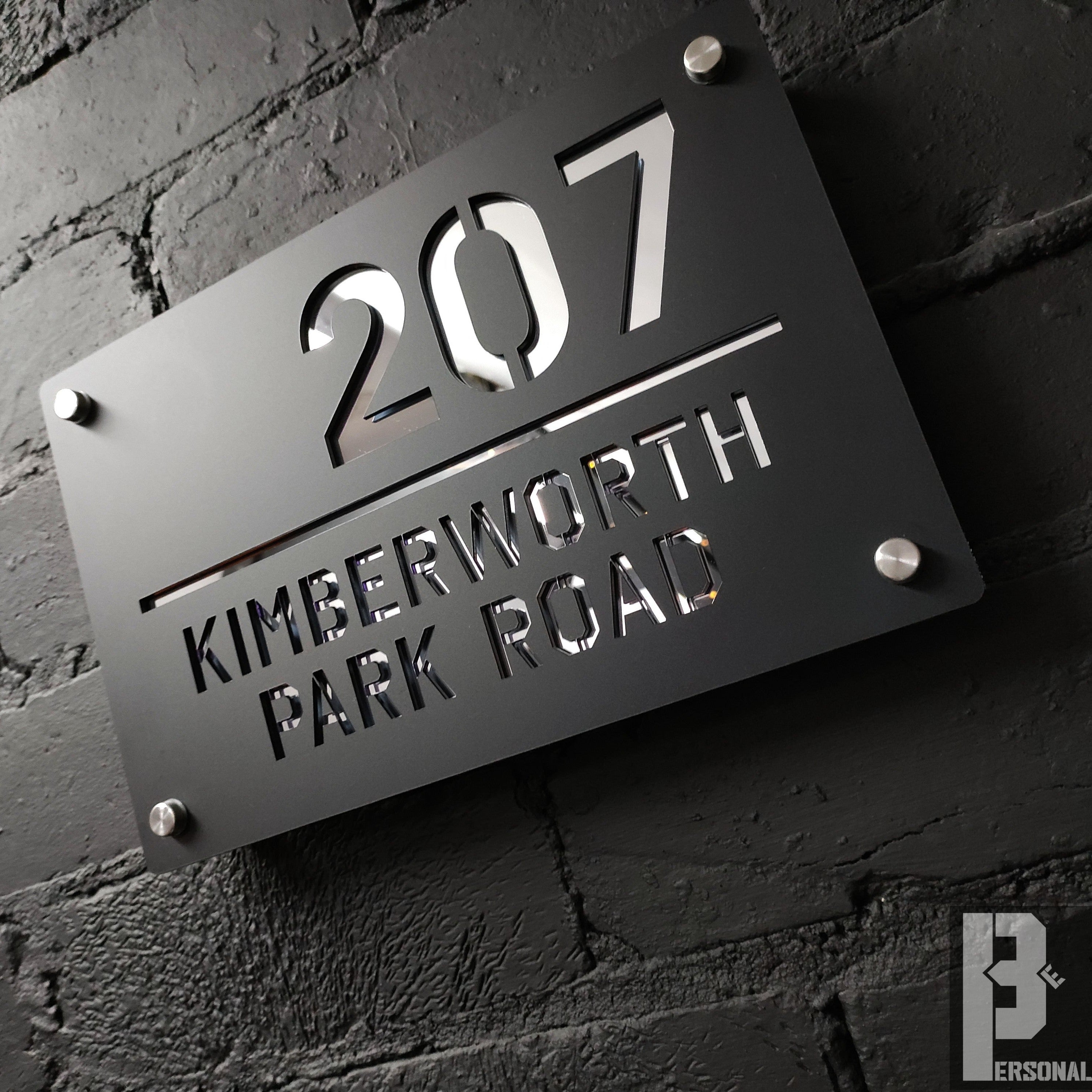 Black metal house sign with 207 Kimberworth Park Road on brick wall