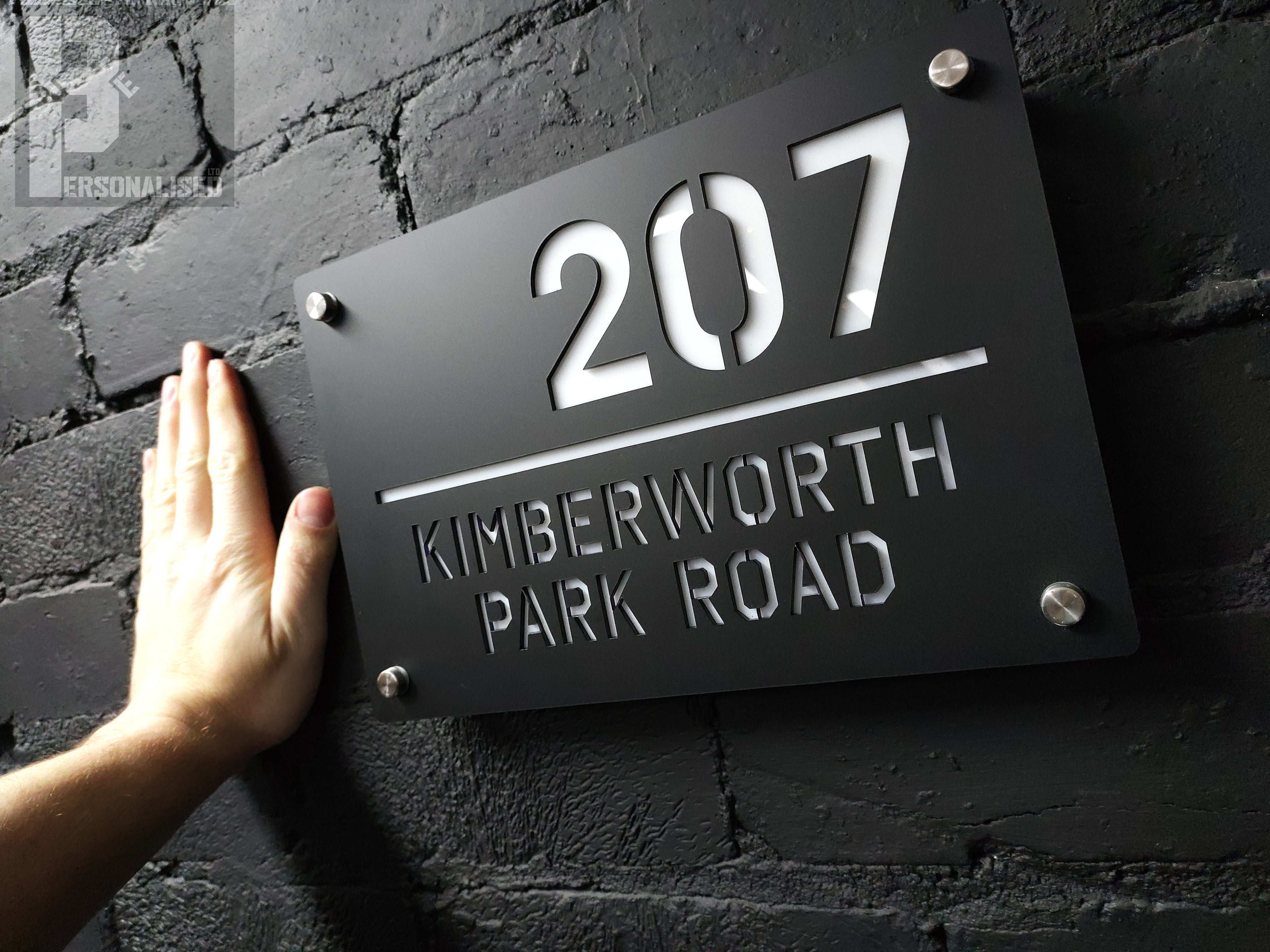 Black metal house sign with 207 Kimberworth Park Road on brick wall